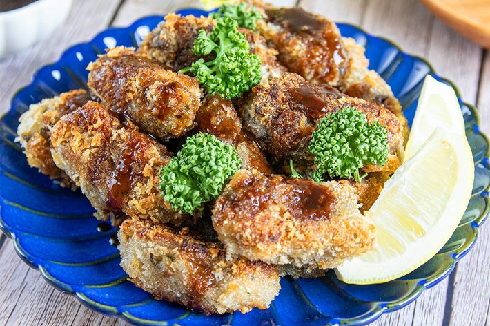 レモンとパセリが添えられた皿に盛り付けられた揚げ物料理。食卓に箸とソースが見える。