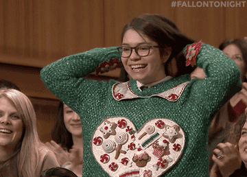 Audience member in a decorated sweater stands smiling with hands on head, while others clap around them on a talk show set