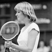 Person in a white tennis dress holding a racket on a tennis court, looking focused
