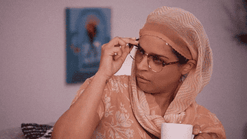 Person with glasses and headscarf looks skeptical while holding a mug