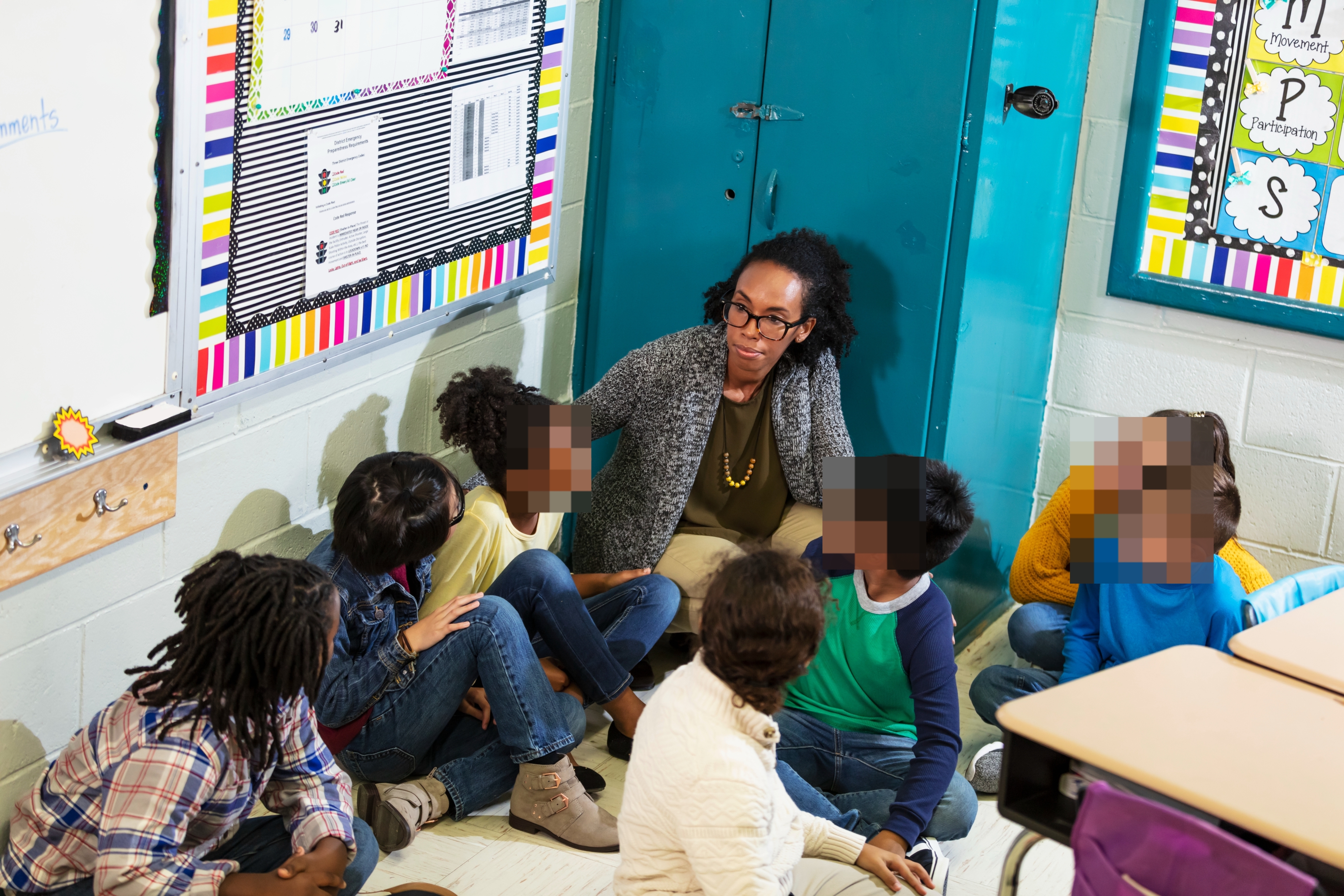 Teacher and diverse group of young students sitting on the floor in a classroom, engaged in a discussion together