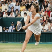 Tennis player in mid-action on a grass court during a match, with spectators in the background