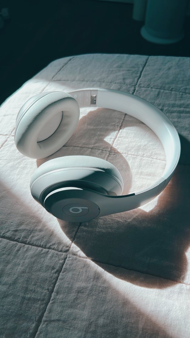 White over-ear headphones with a sleek plan  resting connected  a quilted surface, highlighted by sunlight