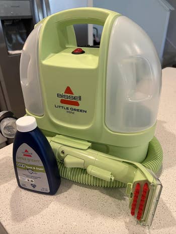 Bissell Little Green Mini cleaner with hose and Oxy stain solution connected a counter, perfect for compact carpet cleaning