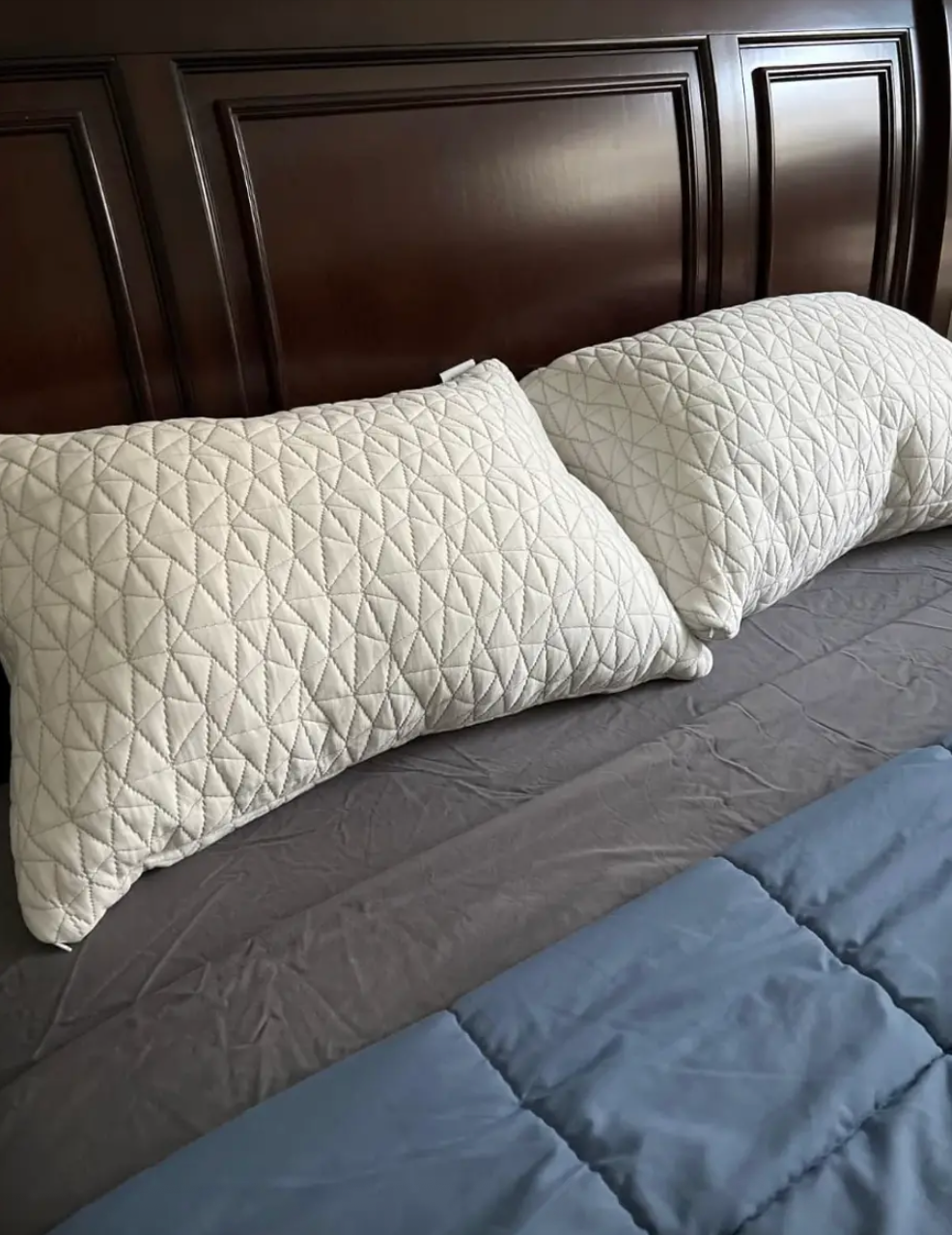 Two quilted pillows rest on a neatly made bed with a headboard, showcasing a comfortable bedding setup