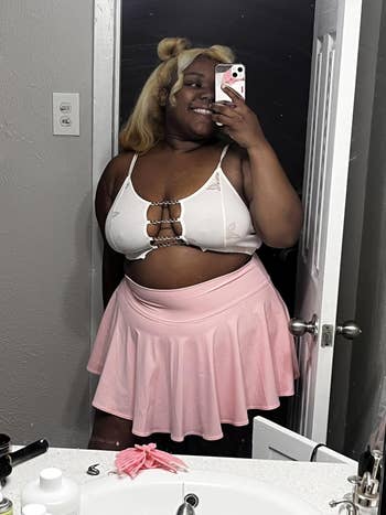 Person smiling successful a reflector wearing a stylish strappy apical and a flared skirt, posing successful a bathroom