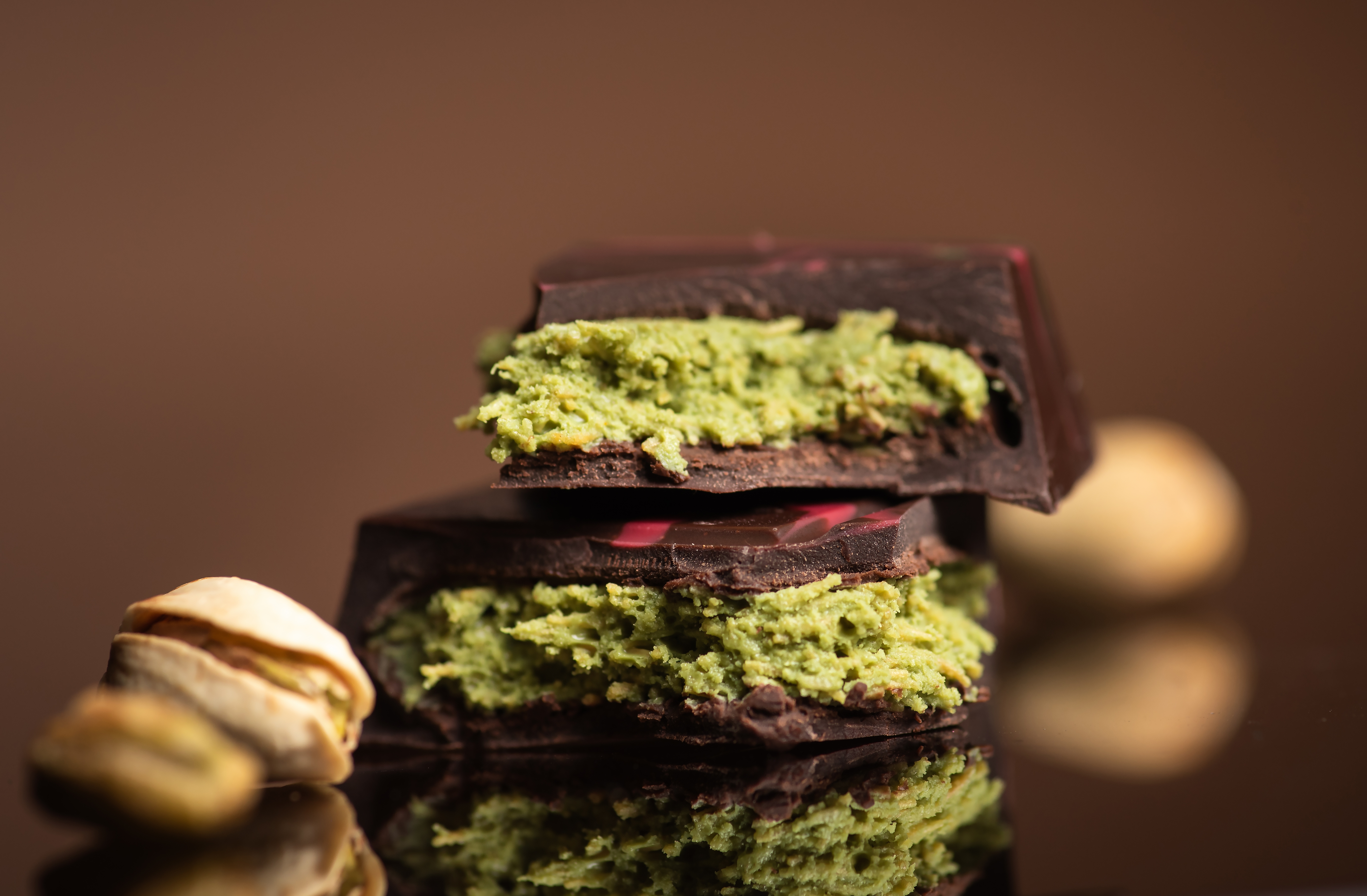 Close-up of dark chocolate pieces with green pistachio filling, beside a couple of pistachios