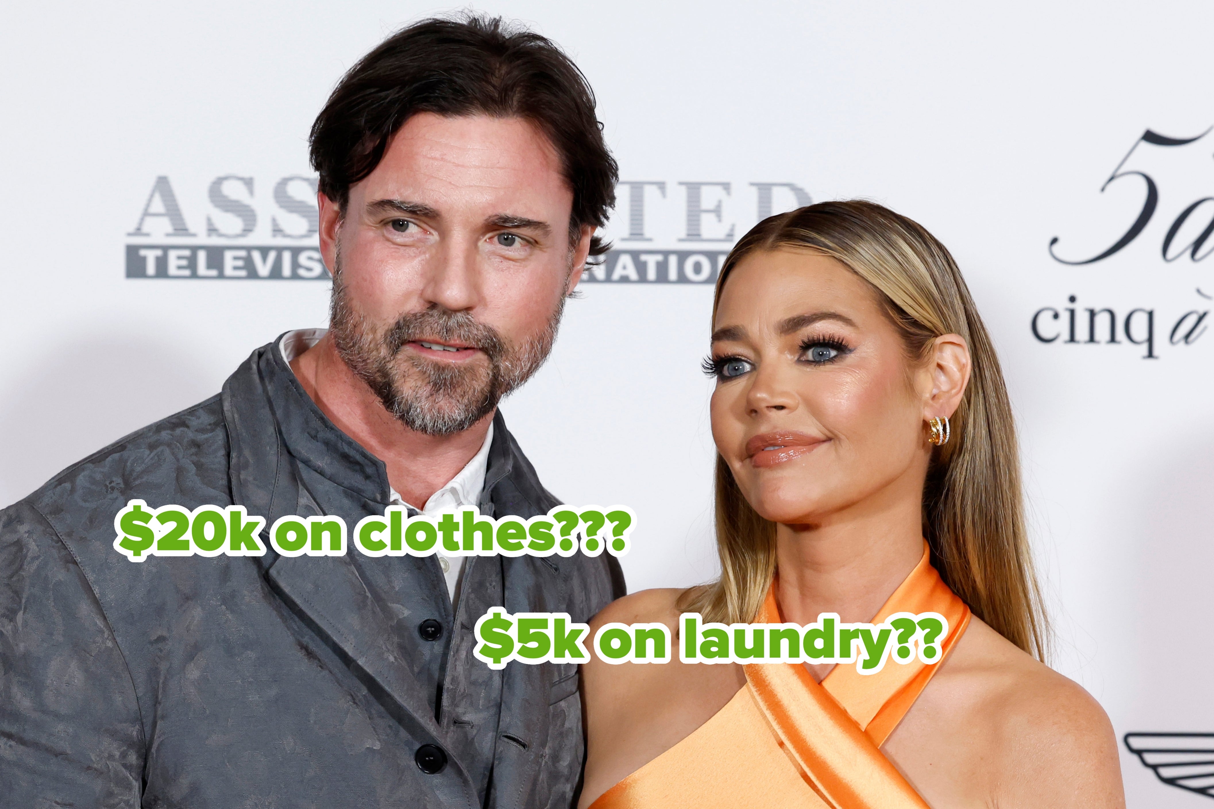 A man in a gray textured suit and a woman in a sleek, orange satin gown pose together at a celebrity event