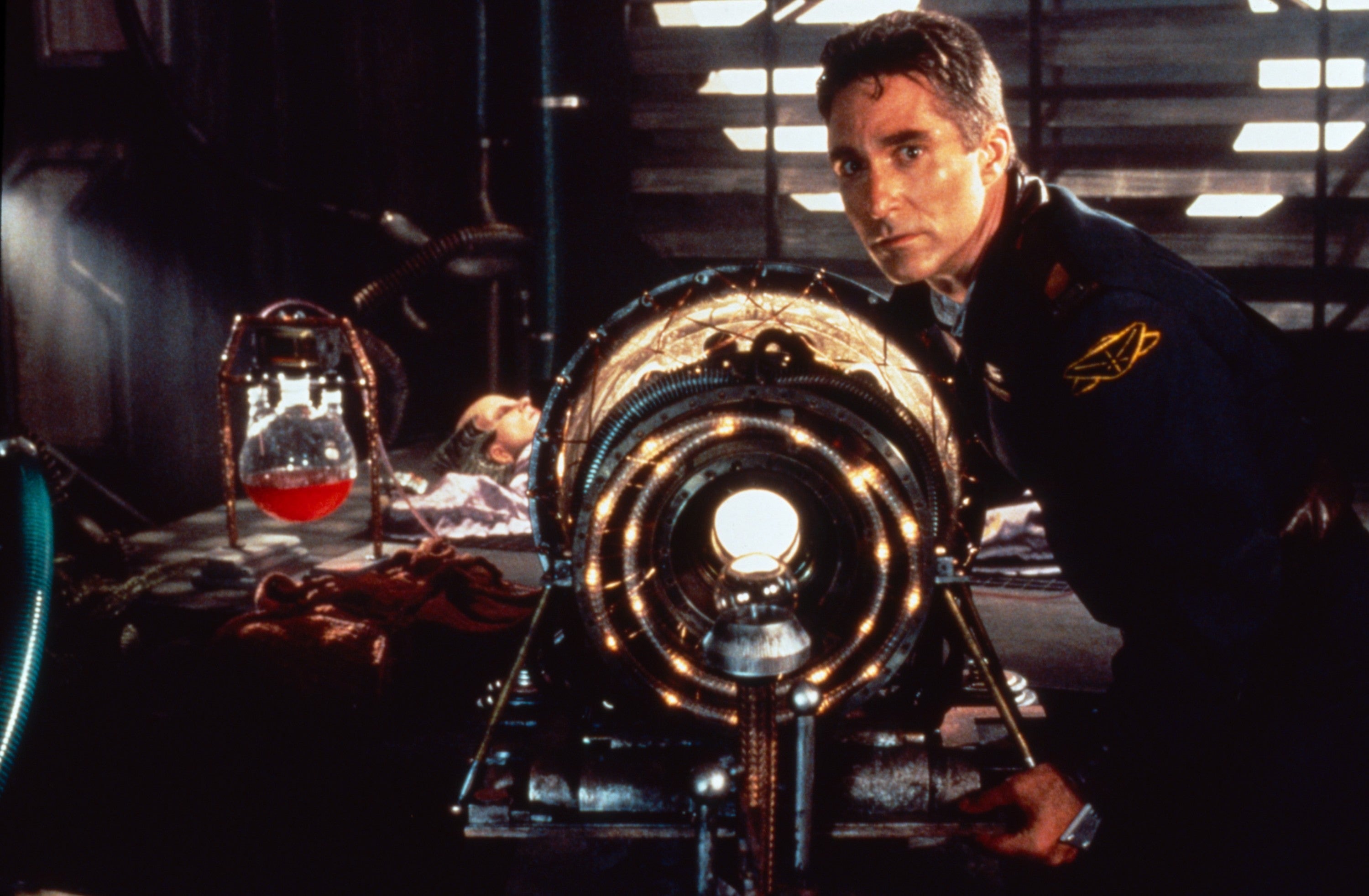 A person in a futuristic setting with a mysterious device, wearing a uniform, looks intently at the viewer, hinting at a sci-fi movie scene