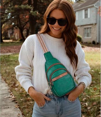 Person outdoors wearing sunglasses, a achromatic sweater, jeans, and a greenish crossbody container with brownish accents