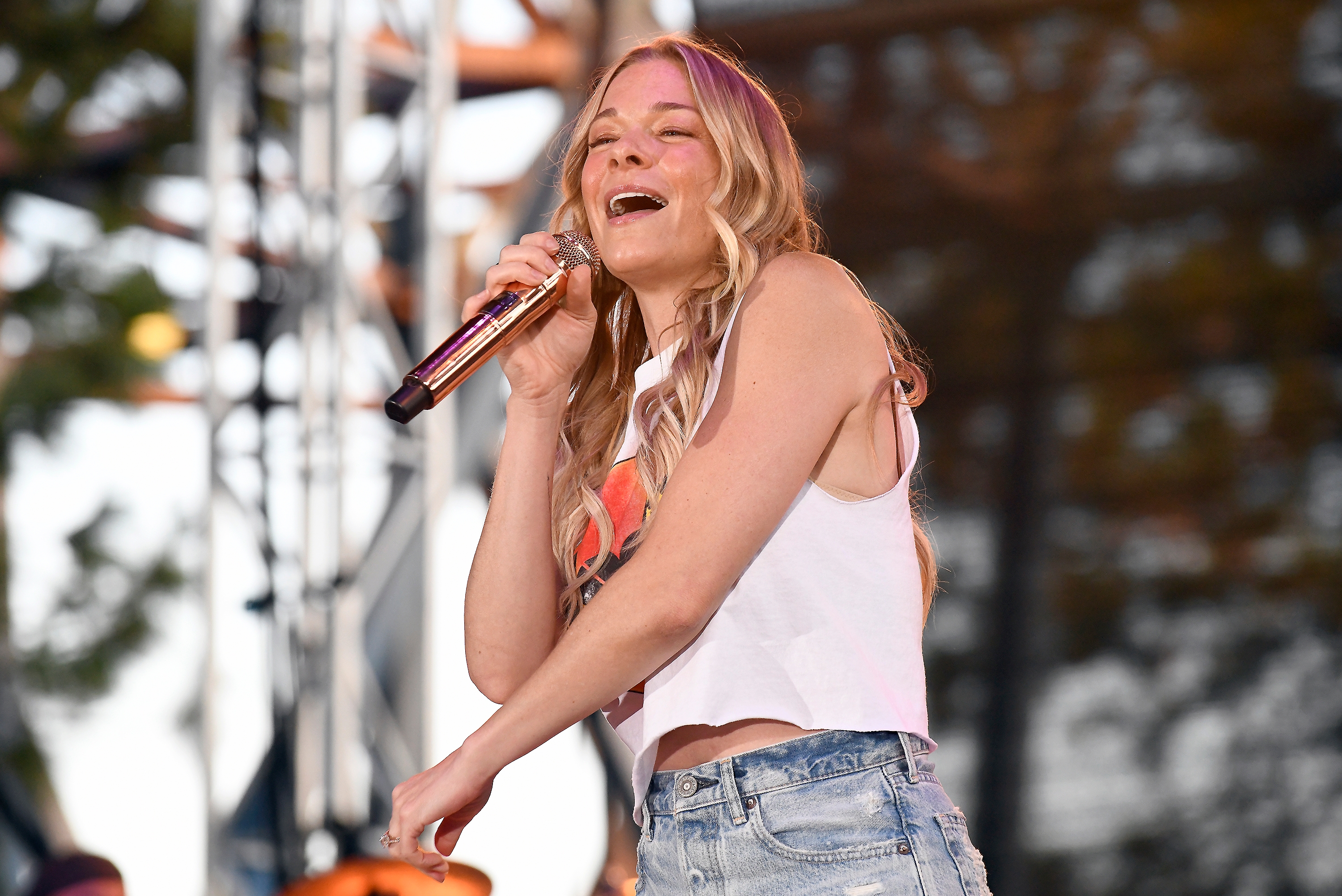 LeAnn Rimes performing on stage, singing into a microphone, wearing a casual sleeveless top and jeans