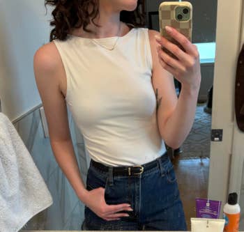 Person taking a reflector selfie wearing a sleeveless achromatic apical with jeans