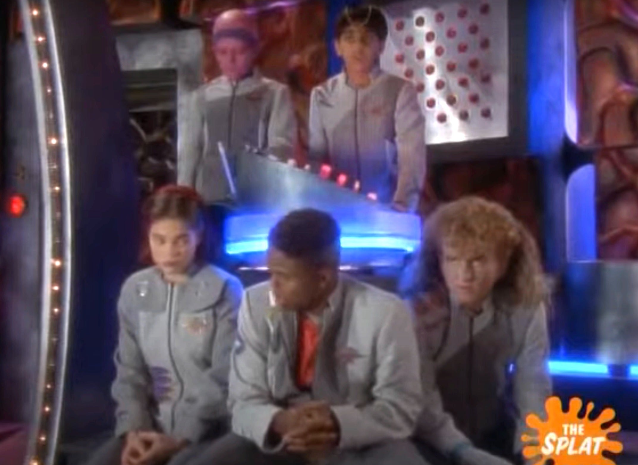 Scene from a sci-fi show with five people in futuristic uniforms inside a spaceship control room