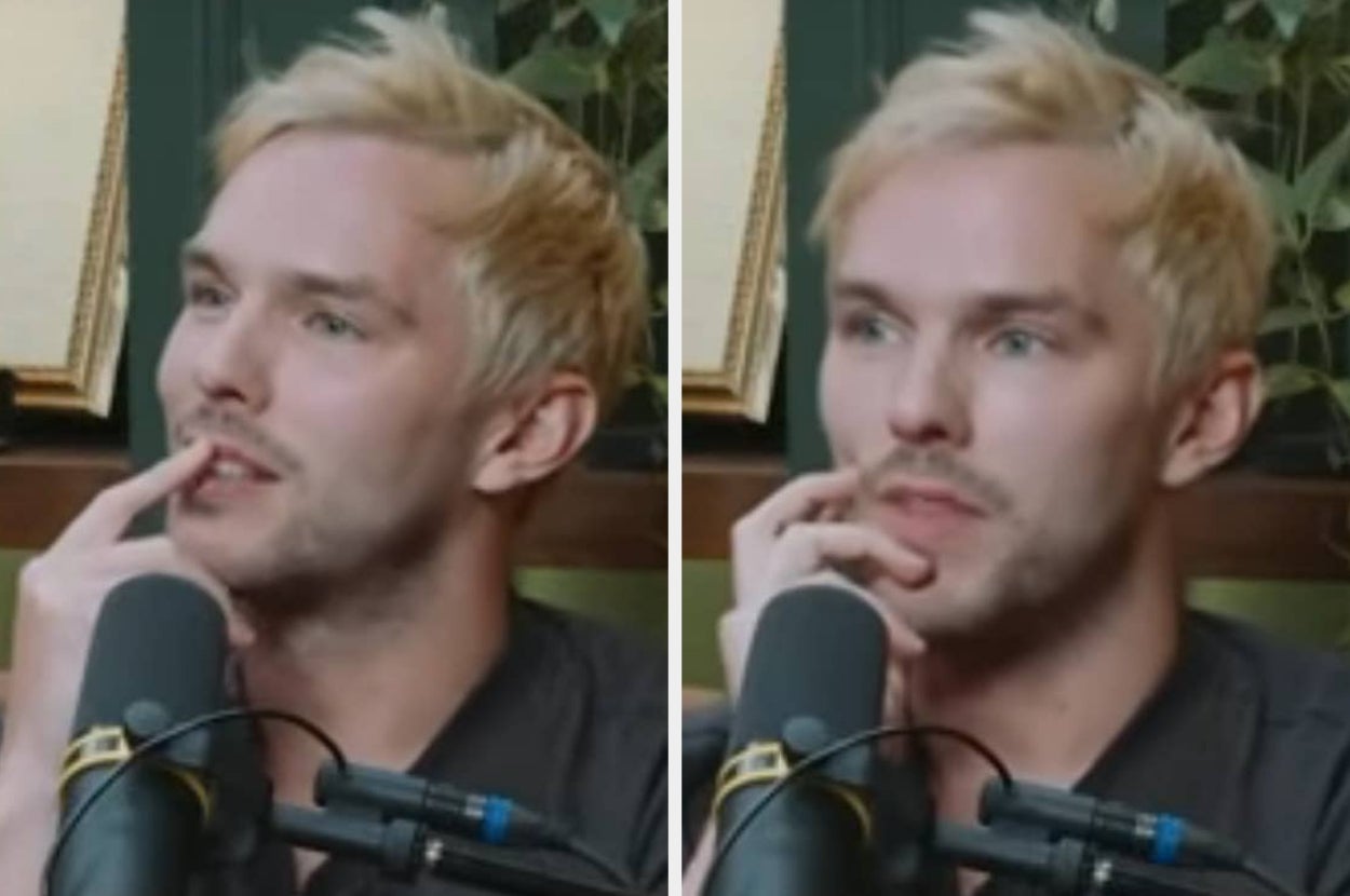 Person with short hair speaking into a microphone, appearing thoughtful with hand on face, in a podcast or interview setting