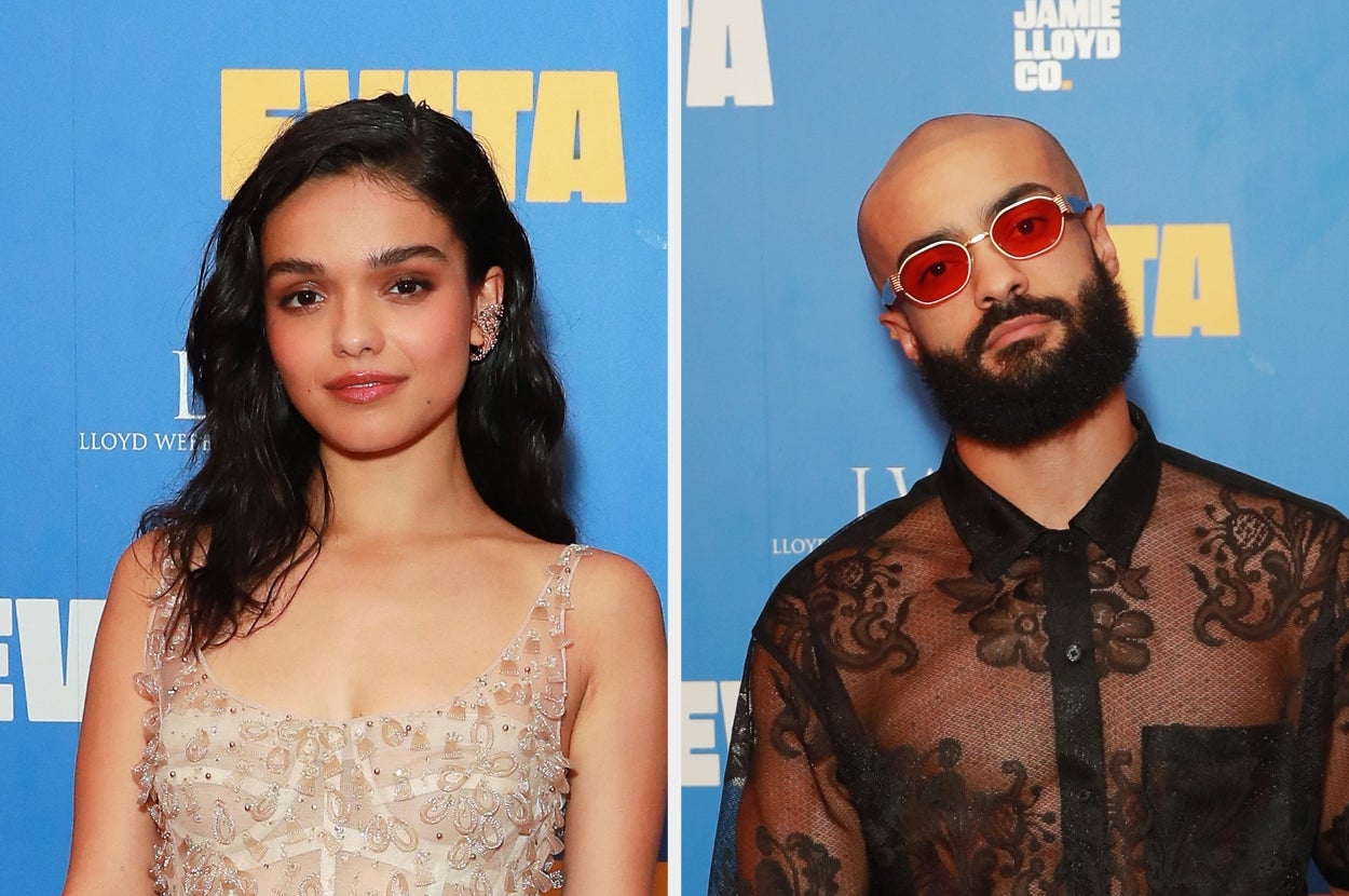 Two individuals pose at an event, one in an elegant sheer dress and the other wearing red sunglasses and a lace-patterned shirt