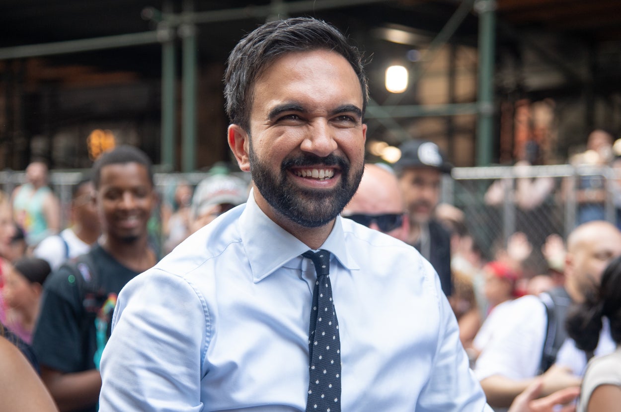 Man in a dress shirt and tie smiling at an outdoor event, surrounded by a crowd of people
