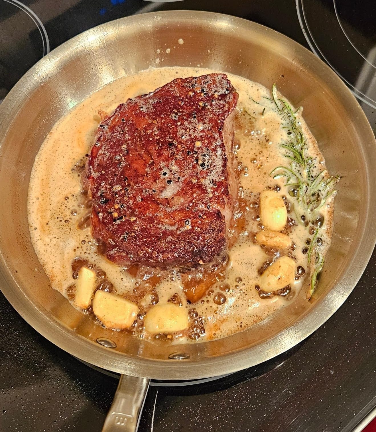 A steak is searing successful  a cookware  with browned butter, ail  cloves, and a rosemary sprig, creating a affluent  and savory aroma