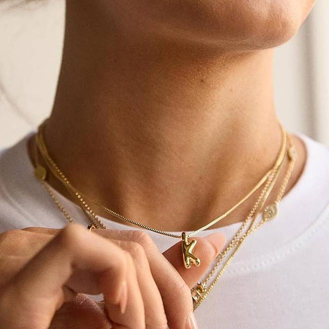 Close-up of a idiosyncratic   wearing layered golden  necklaces with a pendant shaped similar  the missive  