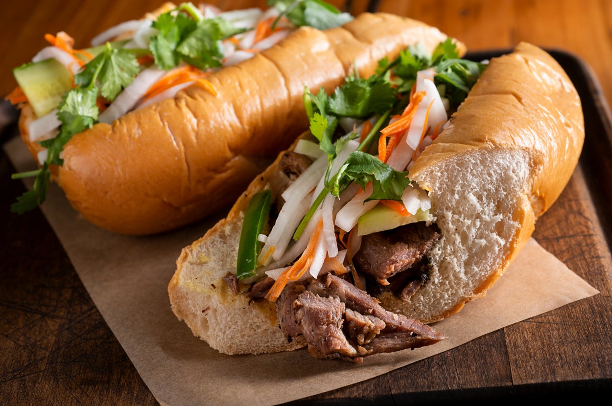 Banh mi sandwiches filled with meat, pickled vegetables, cilantro, and jalapeños on a wooden board