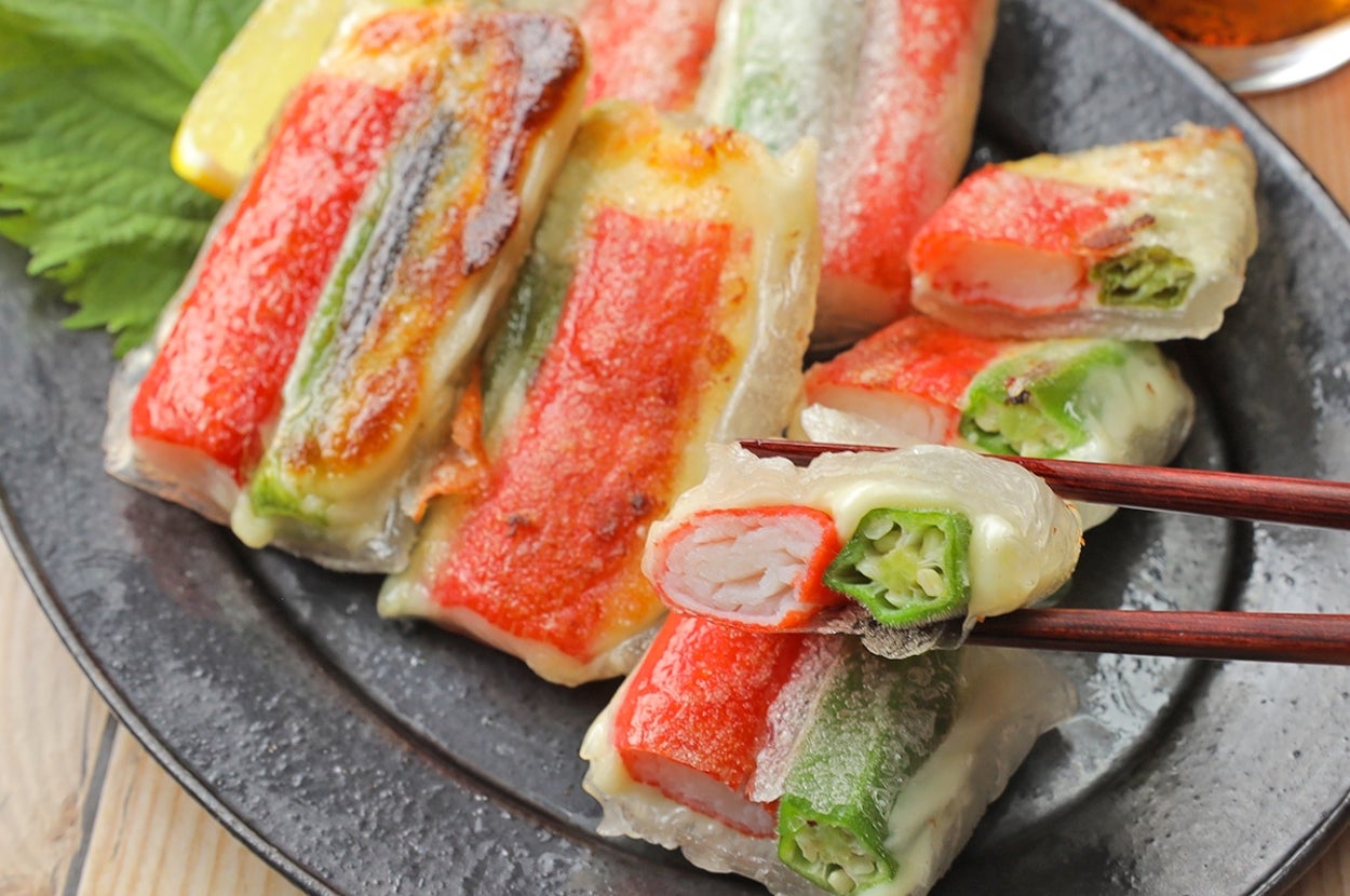 皿に盛られた春巻き風に包まれた野菜とカニカマ、箸で一つ持ち上げている。