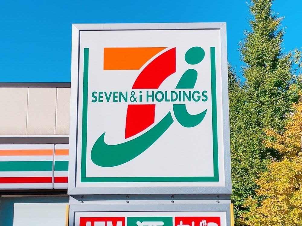 セブン＆アイ・ホールディングスの看板が店舗外に設置されている。背景に樹木が見える。
