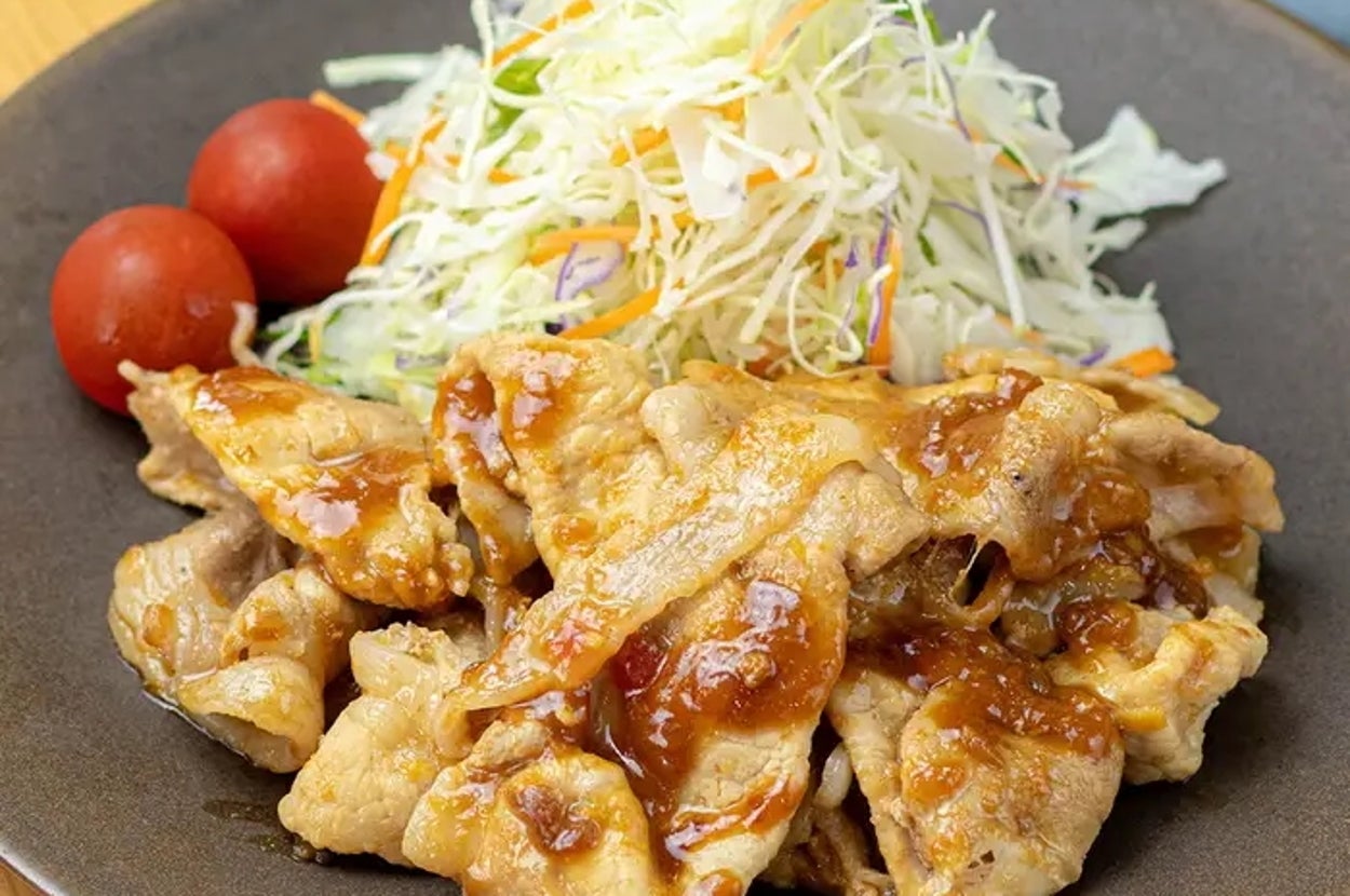 薄切り豚肉の炒め物がプレートに盛り付けられ、細切りキャベツとプチトマトが添えられている。