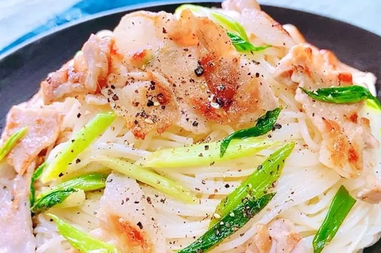 皿に盛られたそうめん、豚肉、野菜がトッピングされ、黒コショウが振りかけられているおいしそうな料理。