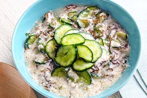 ボウルに盛られたライスとキュウリの料理、クリーミーなトッピング添え。木製のスプーンが横に置かれている。