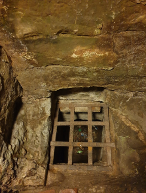 A small, barred window in a stone wall, possibly part of a historical or ancient structure