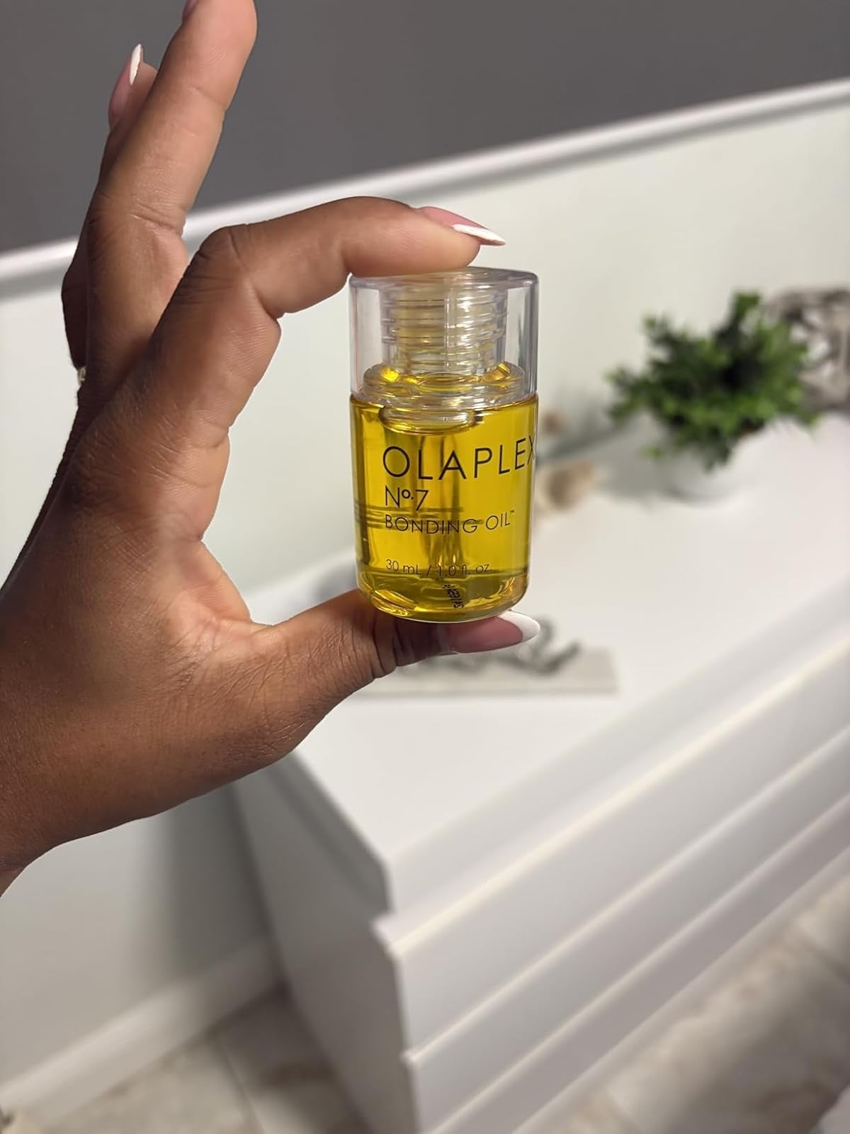 A manus  holds a tiny  vessel  of Olaplex No.7 Bonding Oil successful  a modern   bath  setting