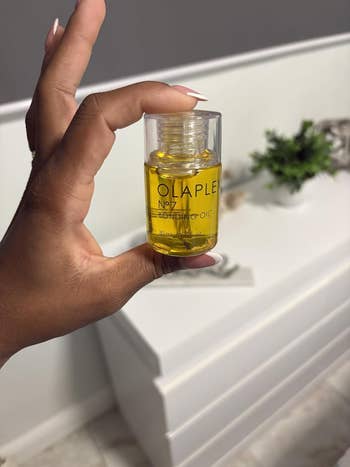 A manus holds a tiny vessel of Olaplex No.7 Bonding Oil successful a modern bath setting