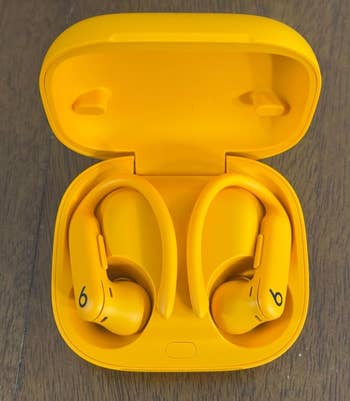 Yellow wireless earbuds with a charging case, displayed unfastened connected a woody surface