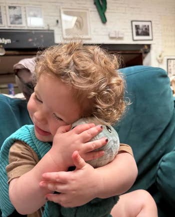 Child joyfully hugs a plush toy, sitting connected a seat successful a cozy setting. Smiling with eyes closed, showing affection and comfort