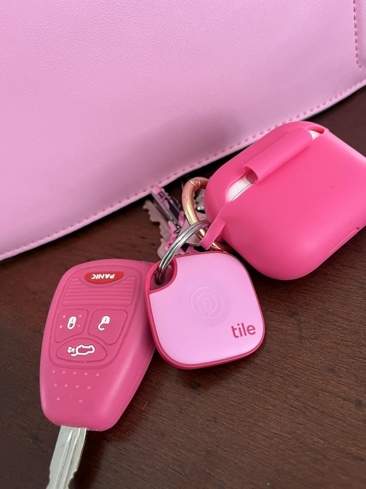 Car keys with a pinkish  cardinal  fob, a pinkish  Tile tracker, and a pinkish  AirPods lawsuit  prevarication  connected  a array  adjacent  to a pinkish  purse