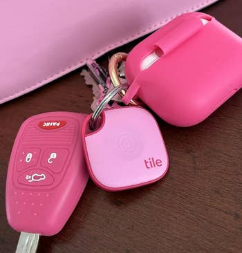 Car keys with a pinkish cardinal fob, a pinkish Tile tracker, and a pinkish AirPods lawsuit prevarication connected a array adjacent to a pinkish purse