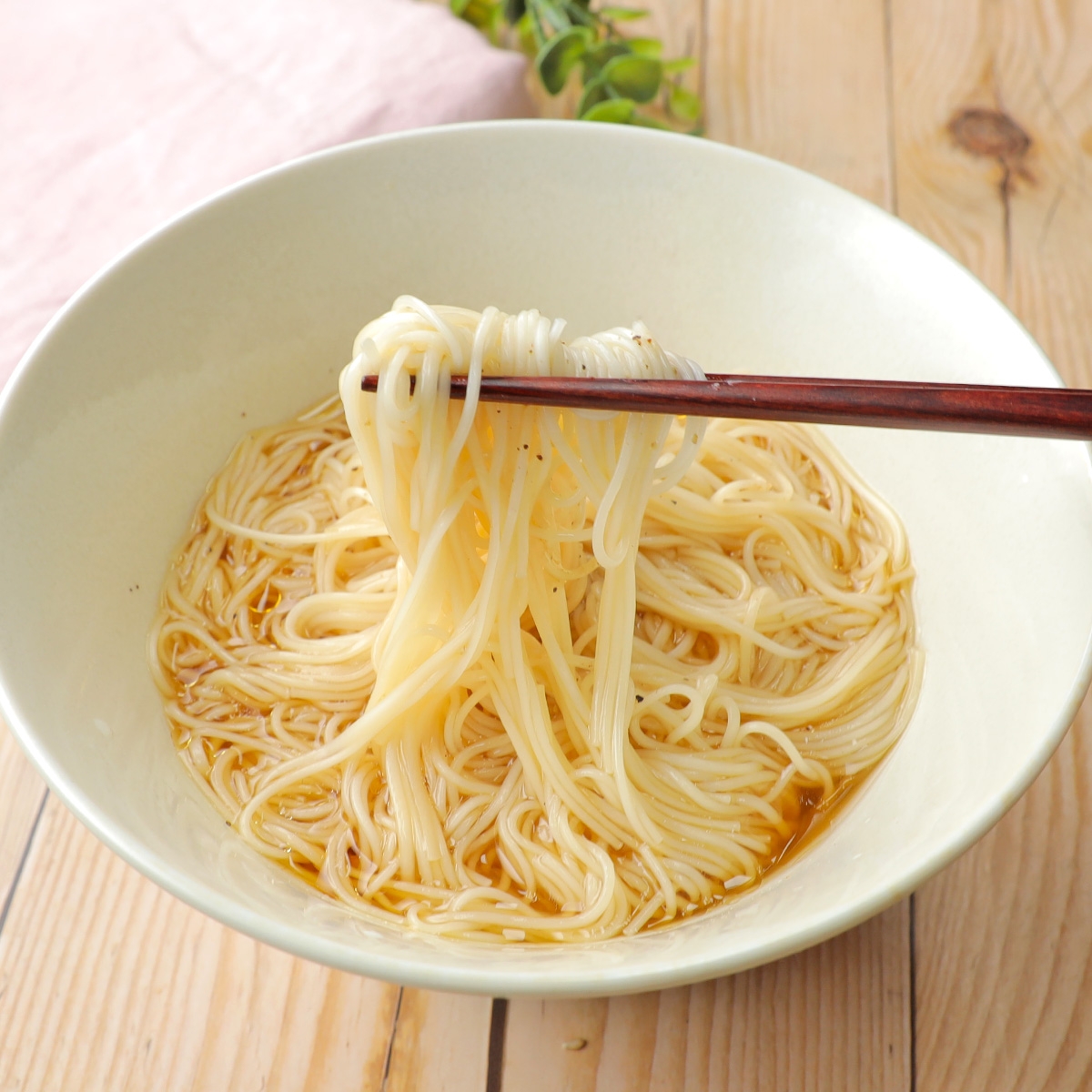 箸で持ち上げた白い麺が入ったボウル。木製のテーブル上。