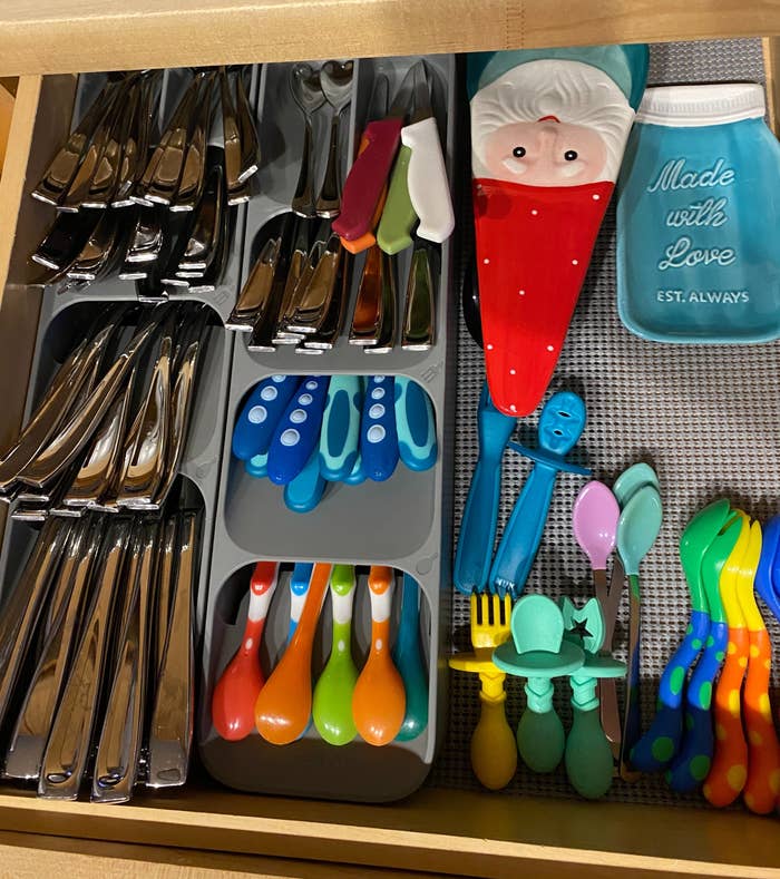 An organized room drawer with neatly arranged cutlery and colorful kids' utensils alongside spatulas and a "Made with Love" jar