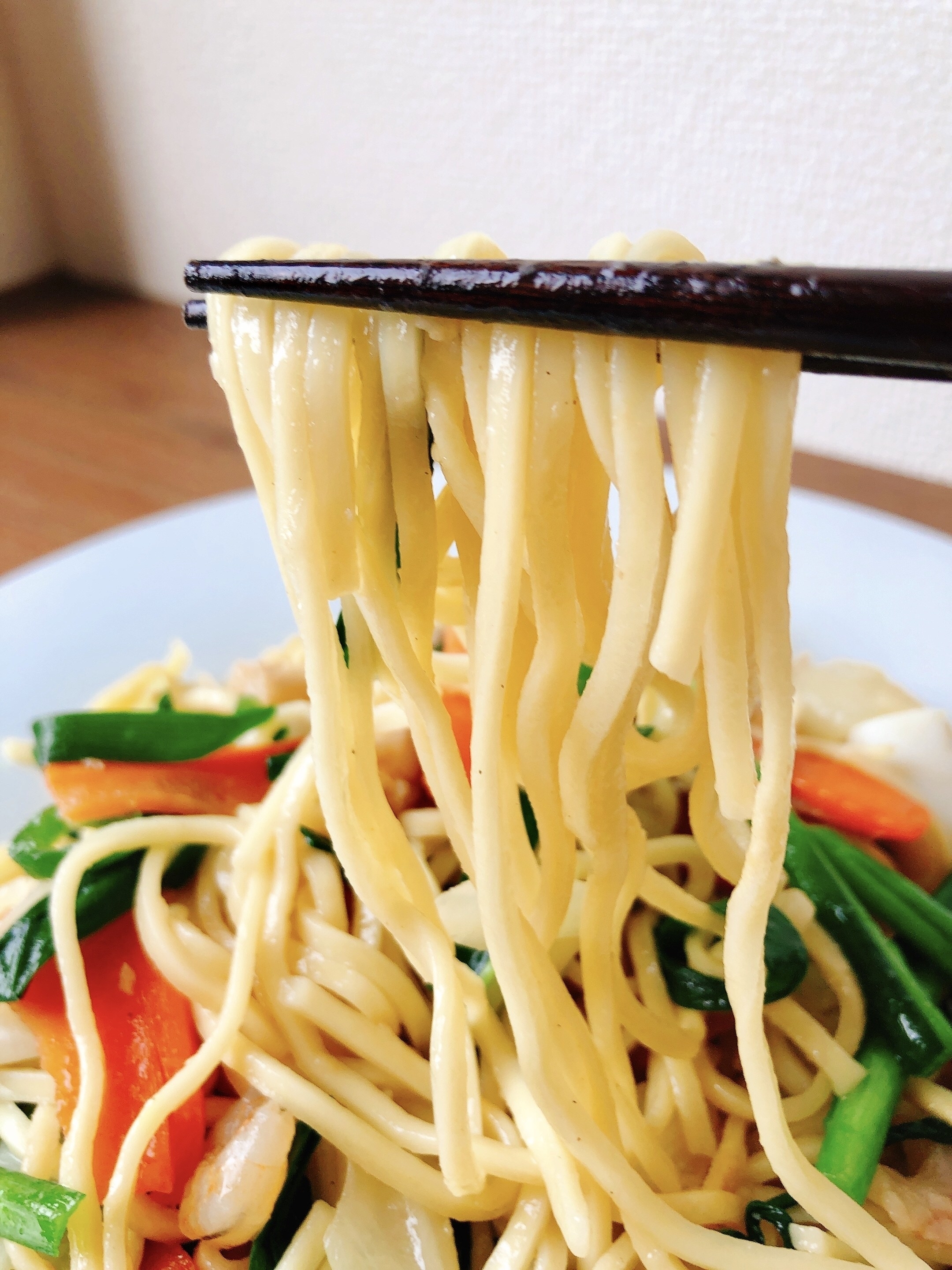 麺を箸で持ち上げる様子。麺には野菜が混ざっている。