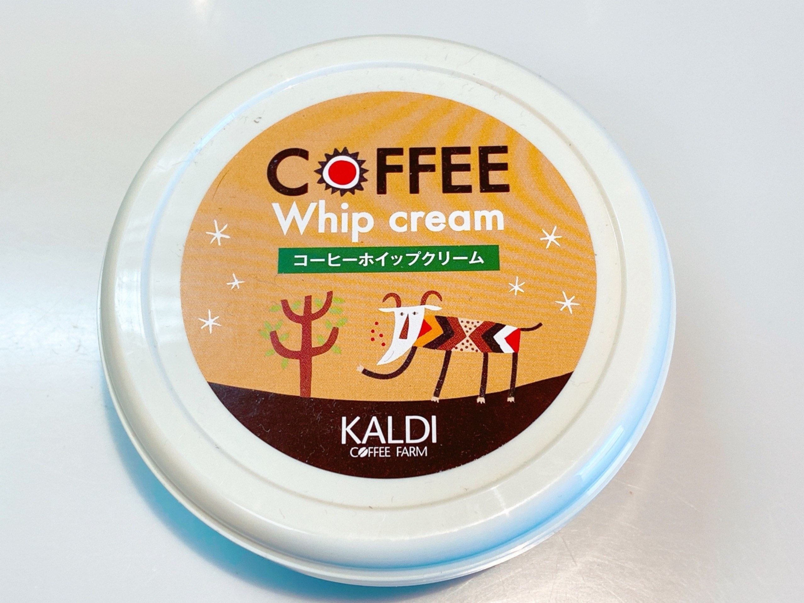 コーヒーホイップクリームの蓋にカラフルなゾウとサボテンのイラスト。コーヒーファームのロゴ入り。