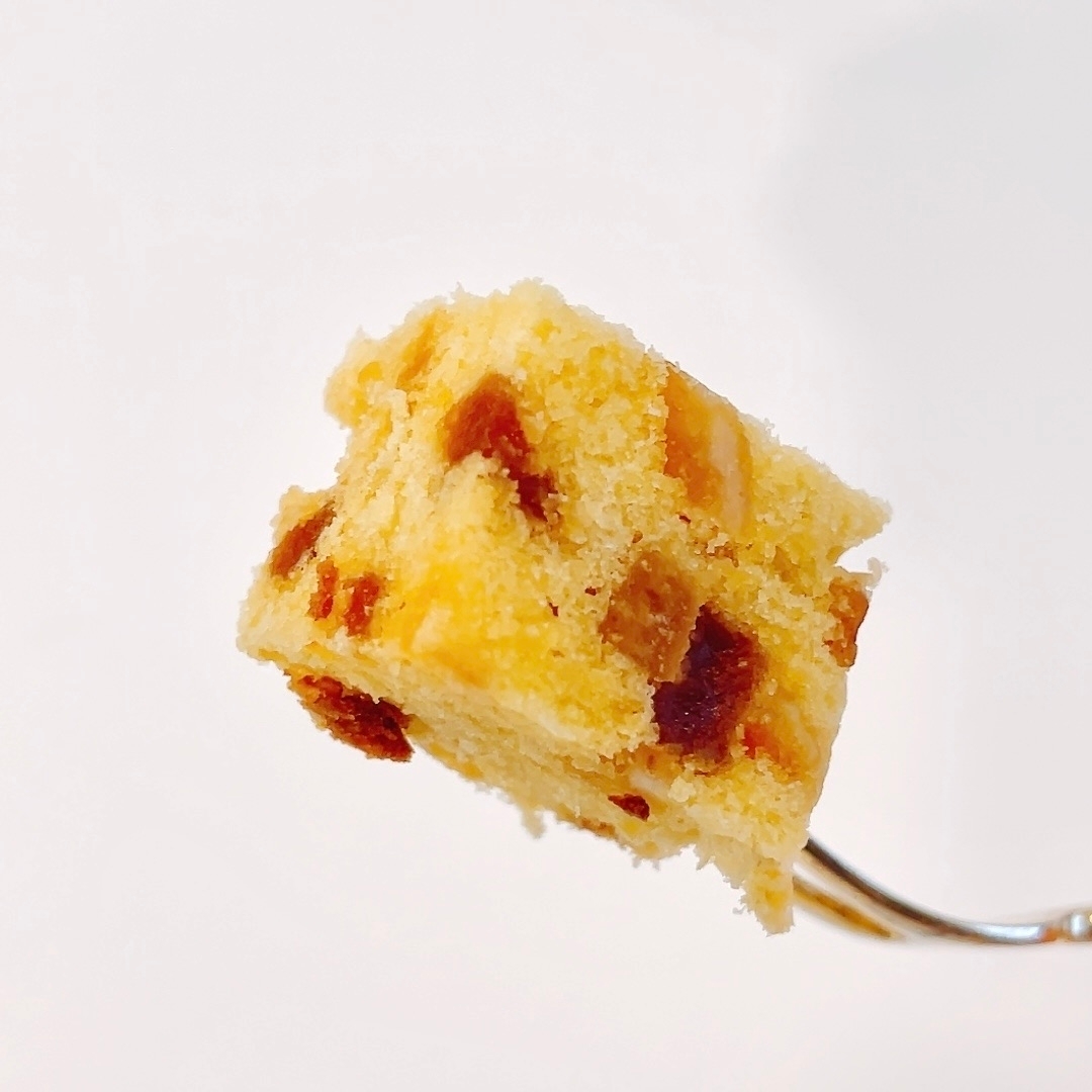 フォークに刺さった一口サイズのケーキ。焼き色の付いた具材が入っている。