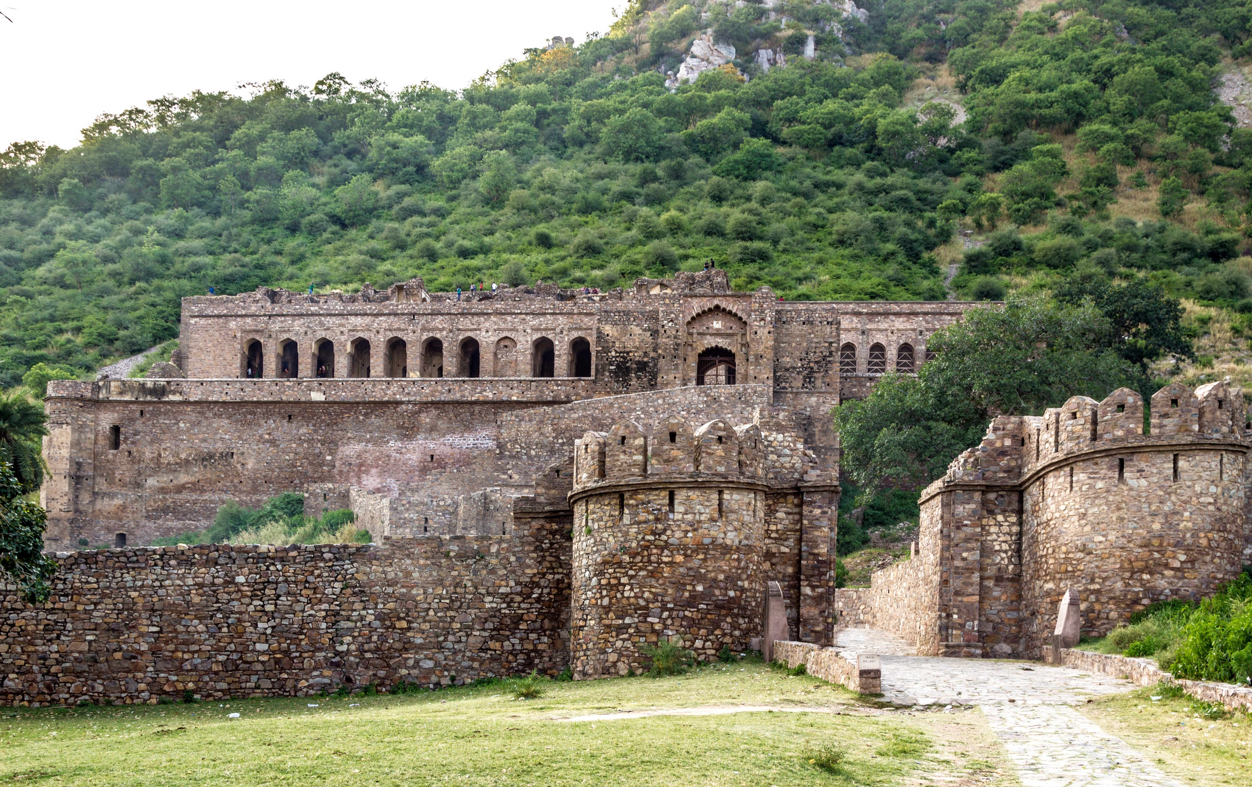 Ancient stone fortress with arched windows and crenelated walls, set among green hills, evoking a sense of history and mystery