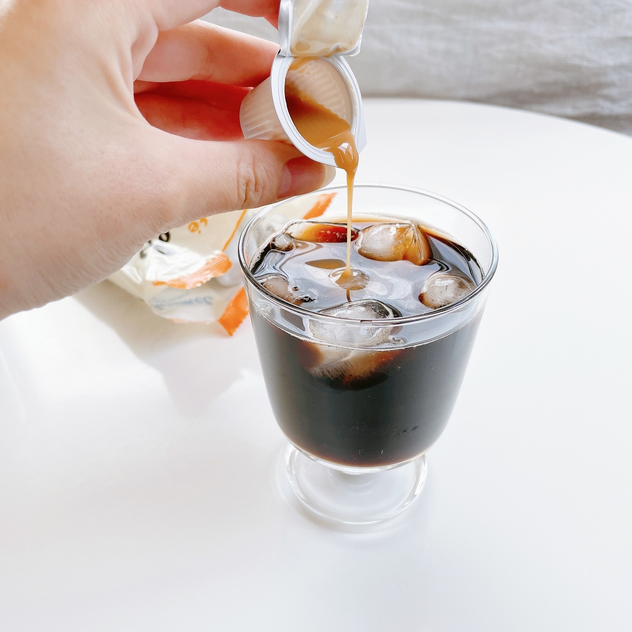 アイスコーヒーのグラスにクリームを注ぐ手。飲み物の広告向けのイメージ。