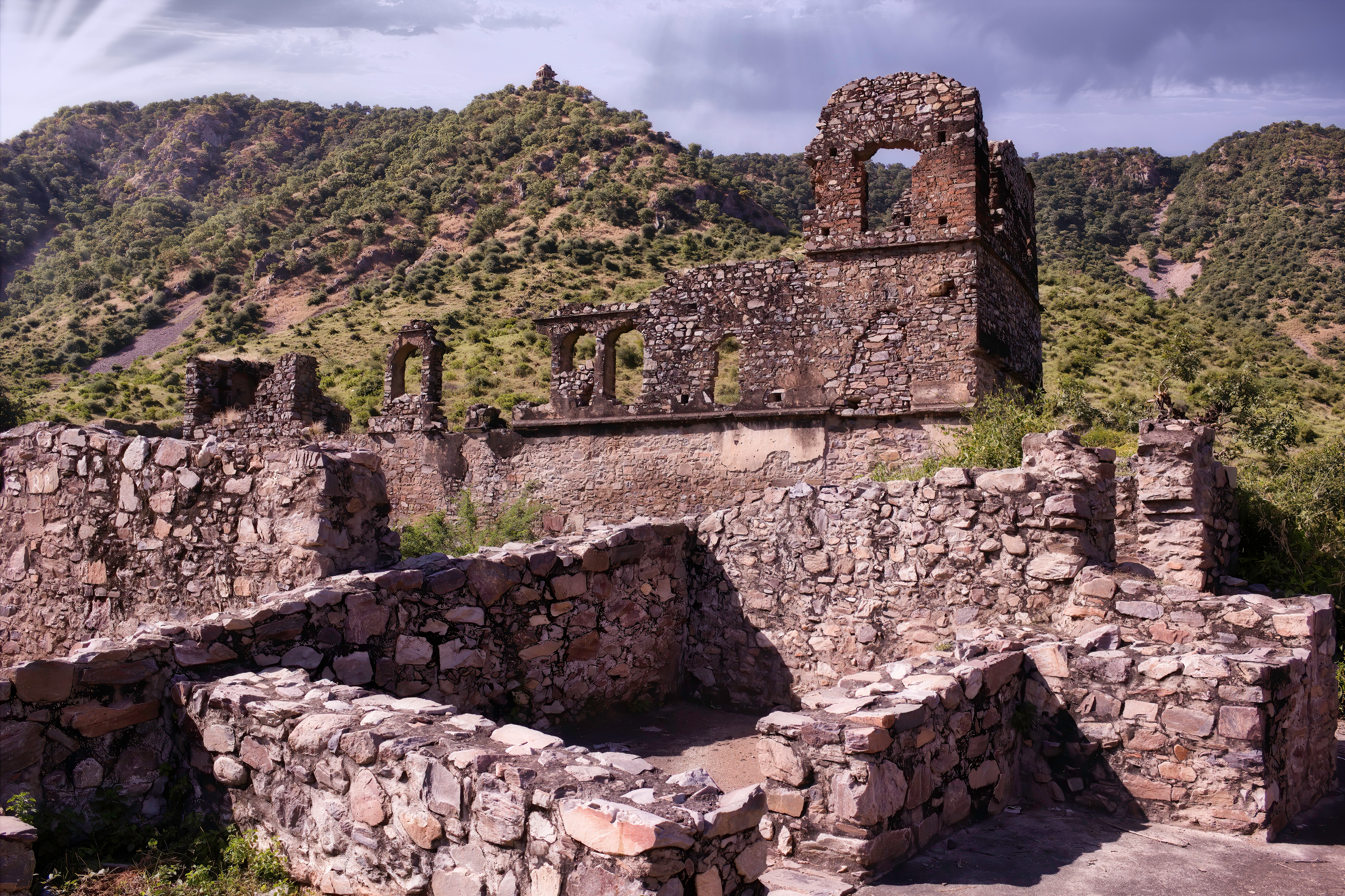 Ancient stone ruins with arches amidst a hilly landscape; overcast sky in the background