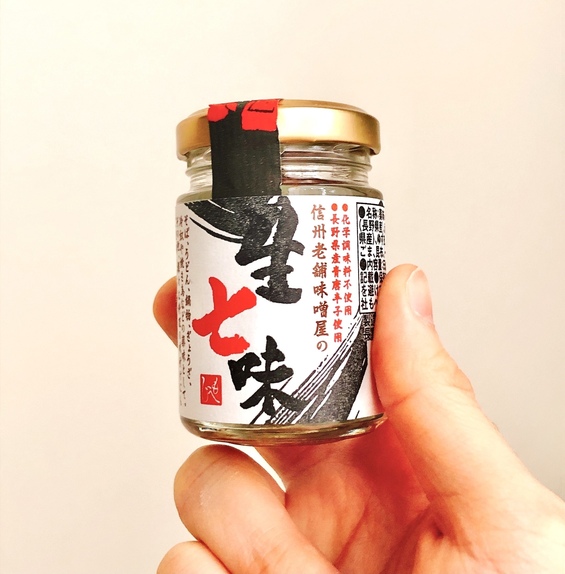 手に持たれたガラス瓶入りの七味唐辛子。ラベルには日本語で商品情報が書かれている。
