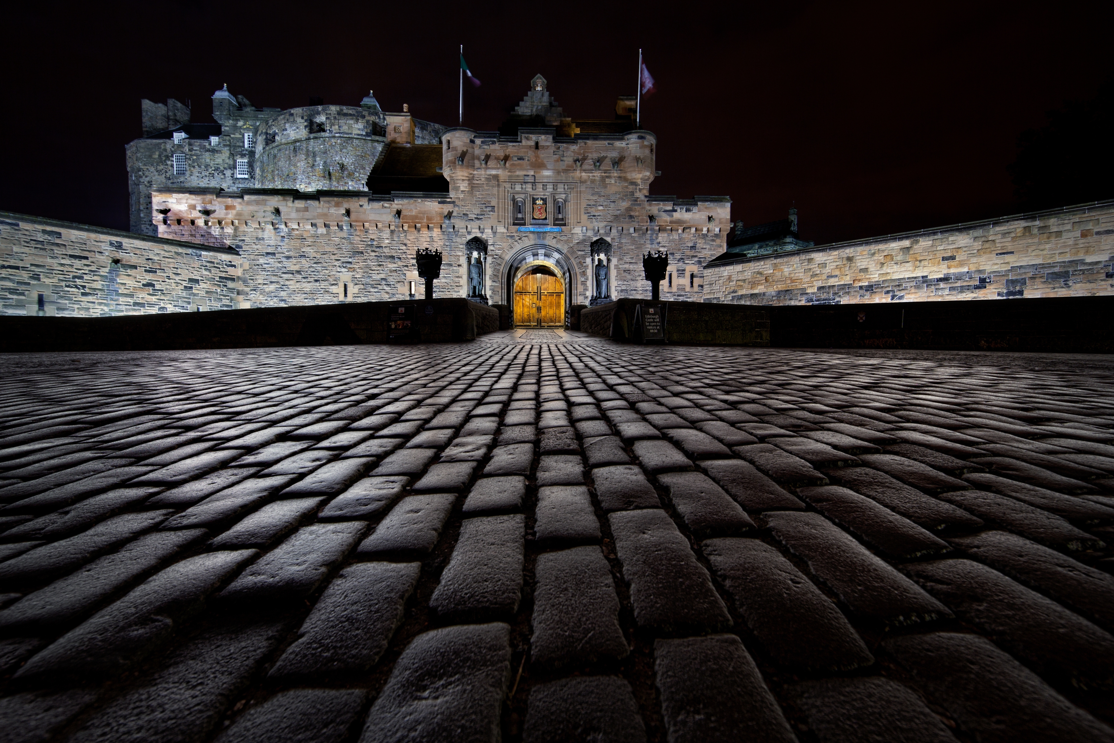 Castle entrance at night with illuminated cobblestone path leading to large wooden doors