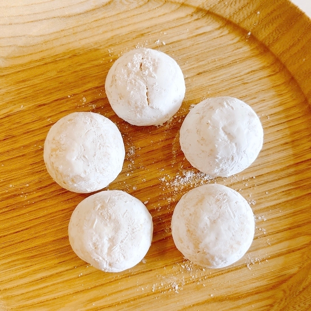木製プレートにのった5つの粉砂糖が振られた小さなドーナツ。