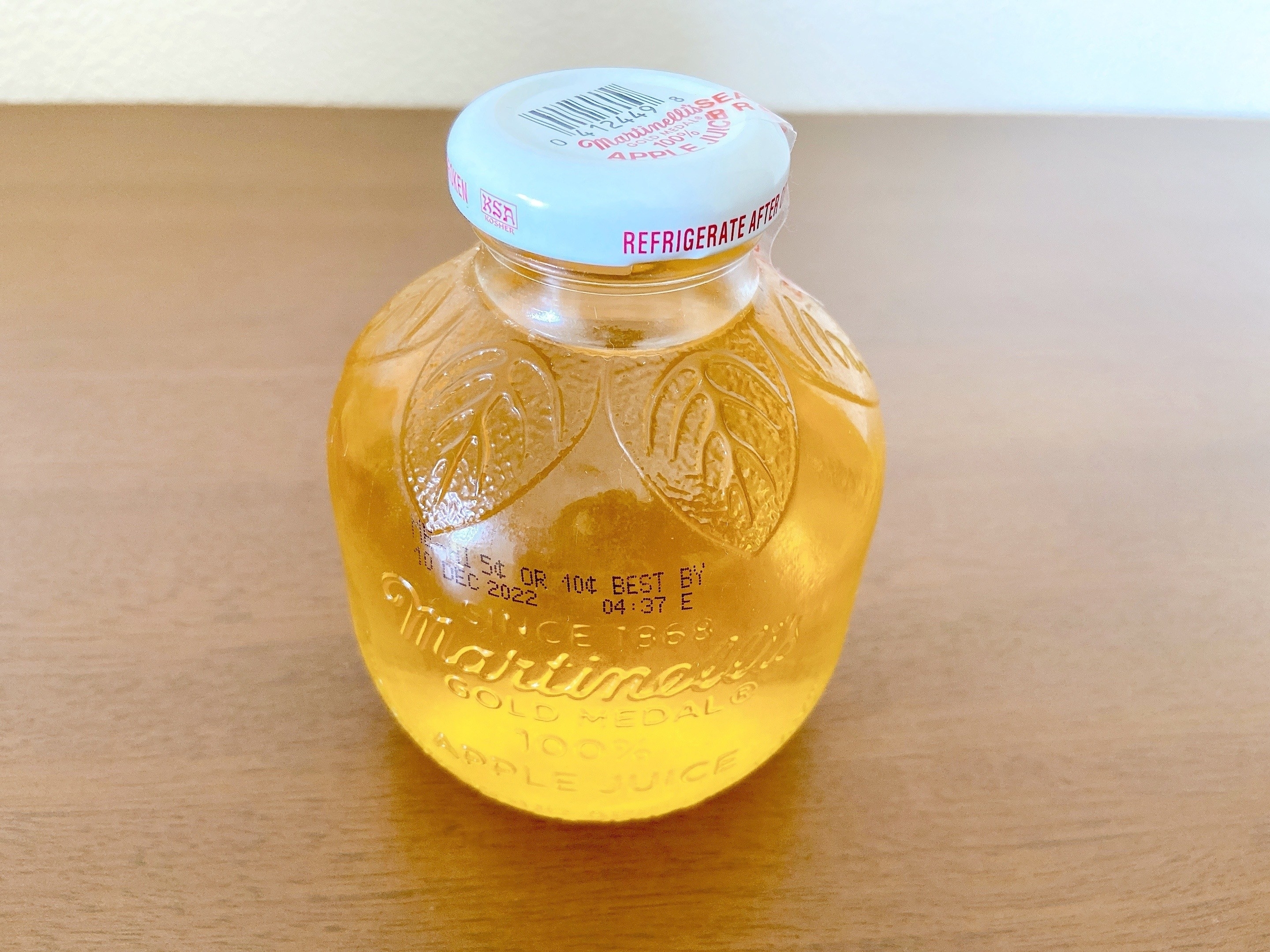 リンゴジュースの透明な瓶。蓋に賞味期限の印字。テーブルの上に置かれている。