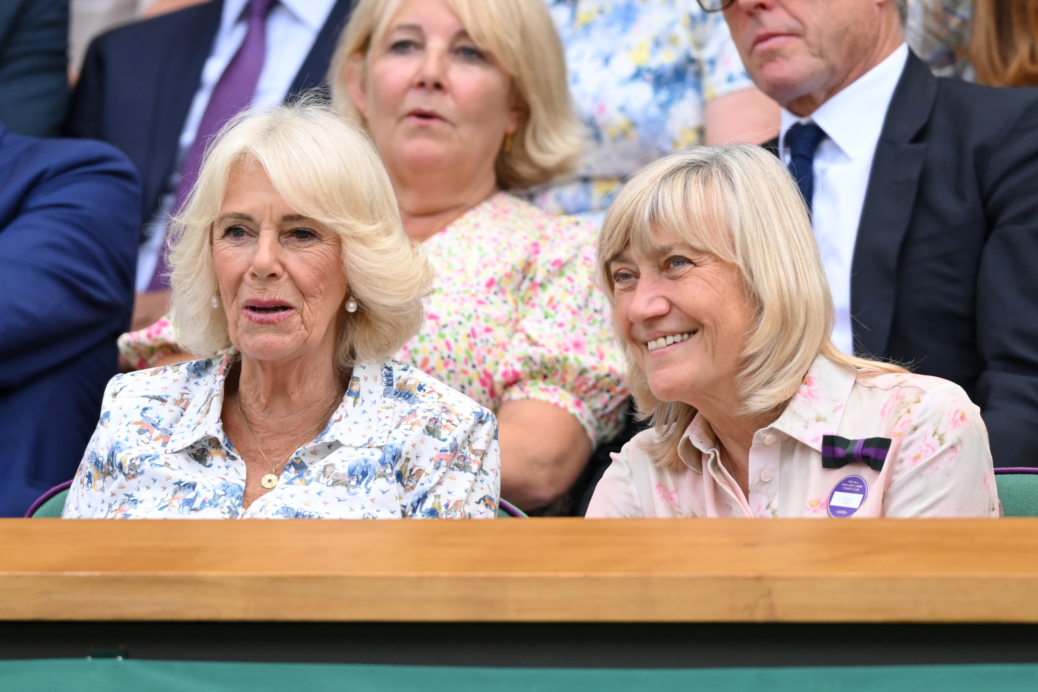 Two women sit in a stadium, both in floral-patterned tops, watching an event