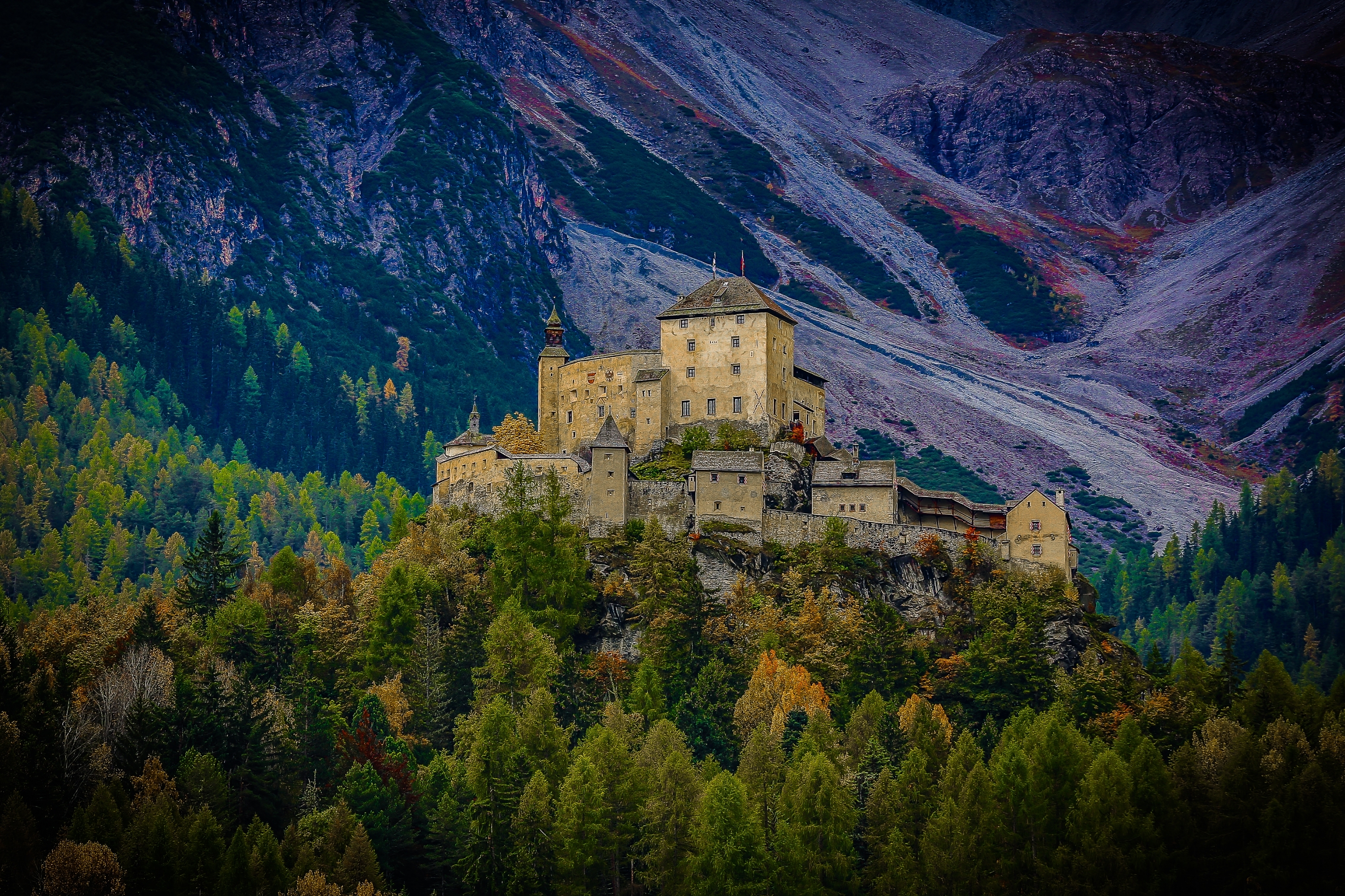 Historic castle atop a forested hill with a mountain backdrop, conveying a sense of grandeur and isolation