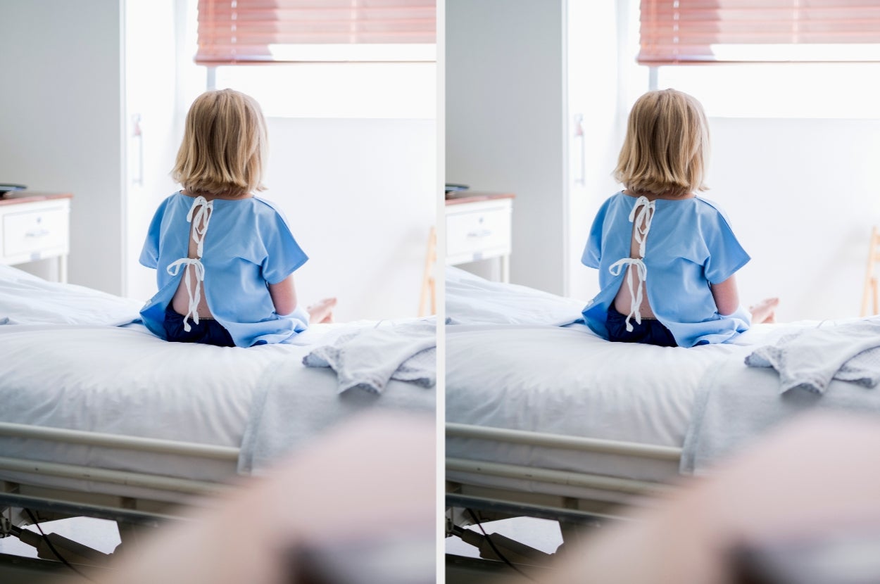 Child in a hospital gown sitting on a bed, looking out the window